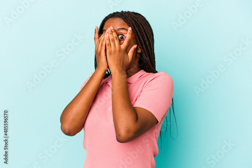 Young african american woman isolated on blue background  blink through fingers frightened and nervous. © Asier