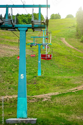Chairlift at the ski resort, view from below. Elevator in the summer season. Moving rope and chairs. Green pine forest in the mountains.