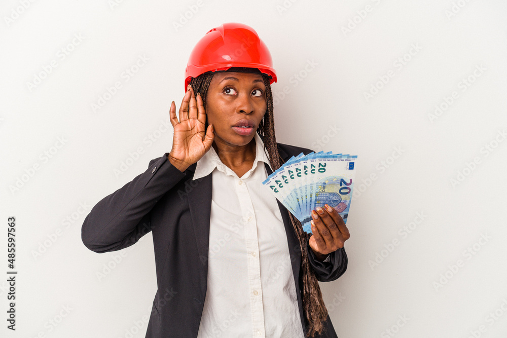 Young african american architect woman holding bills isolated on white background trying to listening a gossip. Young african american architect woman holding bills isolated on white background trying to listening a gossip.