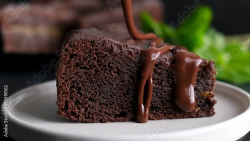Pouring chocolate glaze on slice of chocolate cake. Delicious brownie cake closeup view