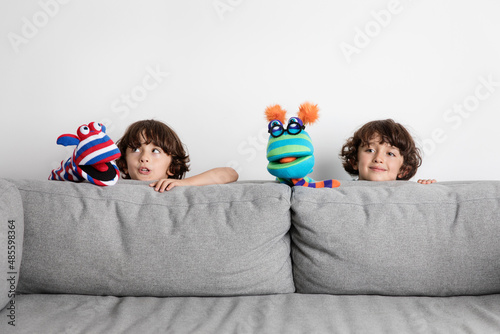 Funny twin brothers making puppet show behind couch photo