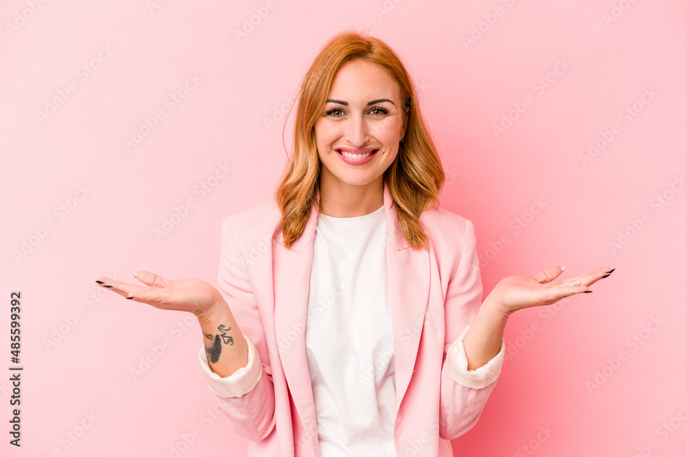 Young caucasian woman isolated on pink background makes scale with arms, feels happy and confident. Young caucasian woman isolated on pink background makes scale with arms, feels happy and confident.