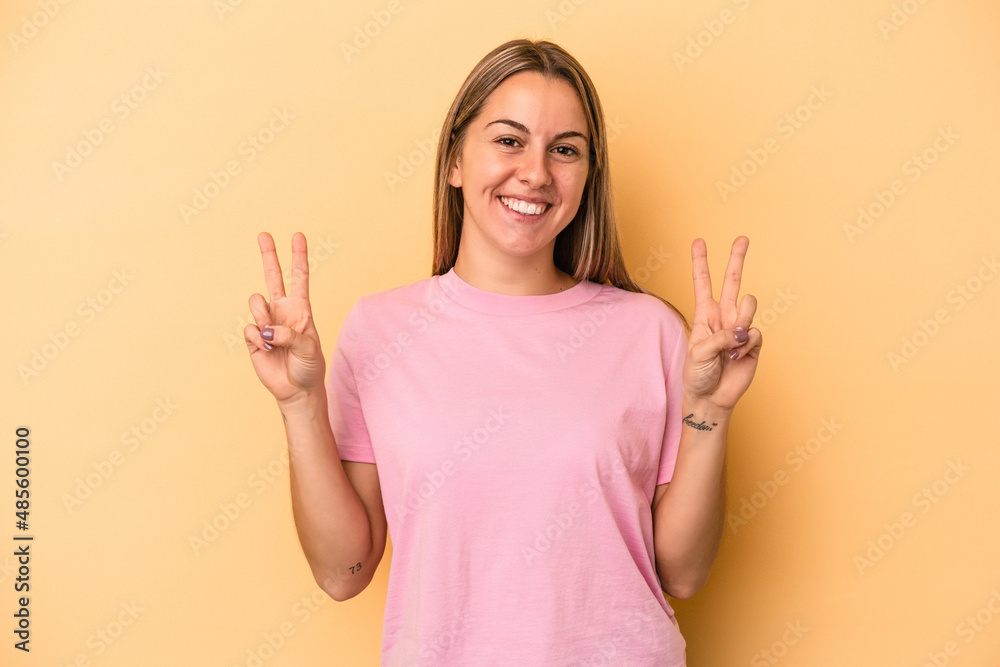Young caucasian woman isolated on yellow background showing victory sign and smiling broadly. Young caucasian woman isolated on yellow background showing victory sign and smiling broadly.