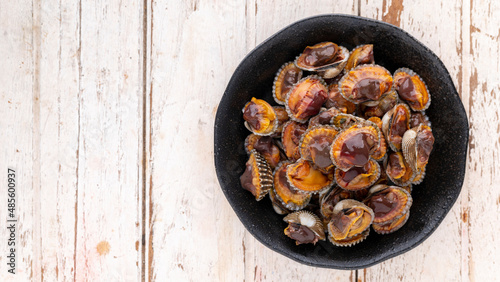 fresh steamed cockles, boiled cockles in black ceramic plate on white wood texture background with copy space for text, top table view, flat lay, blood cockle