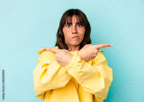 Young Argentinian woman isolated on blue background points sideways  is trying to choose between two options.