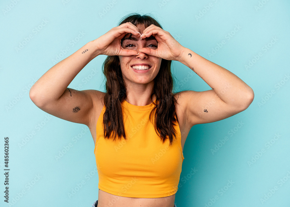 Young Argentinian woman isolated on blue background showing okay sign over eyes