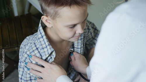 a doctor with a turquoise manicure listens with a stethoscope to the chest of a teenager girl unbuttoning his shirt photo