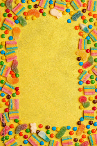 Colorful assortment of candies in shape of frame on yellow background. Top view, copy space