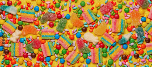 Colorful assortment of candies on yellow background. Top view, banner
