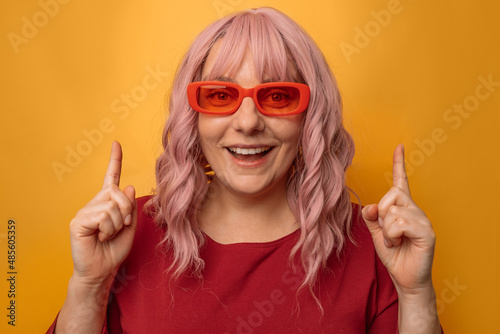 Portrait of attractive caucasian woman raises finger up, showing copy space, spreading information isolated on pink background