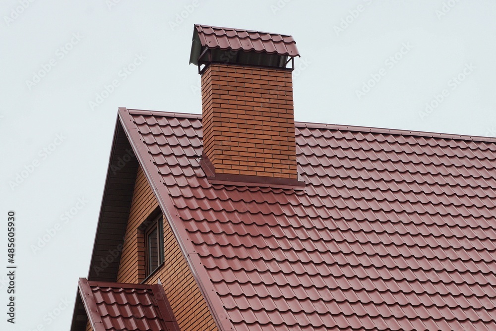 one large red brick chimney on the tiled roof of a private house against a gray sky