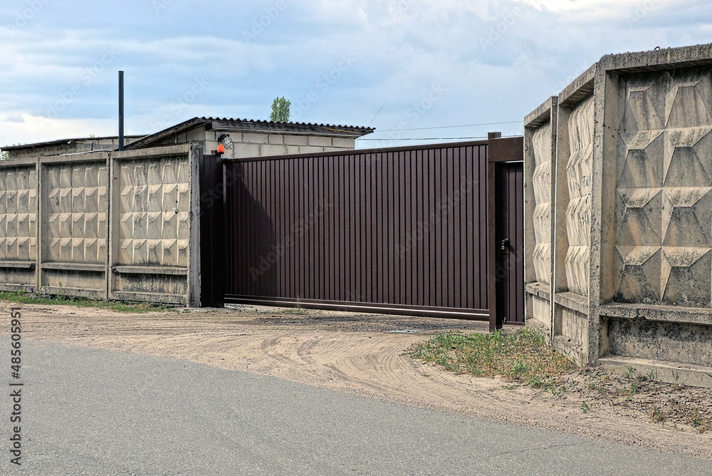 Fototapeta premium one closed brown metal gate and part of a gray concrete wall fence on the street