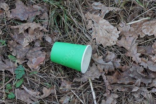 garbage from one green paper cup lies on grass and dry brown leaves in nature