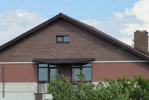 brown brick attic of a private house with an iron balcony with windows on the street against a blue sky