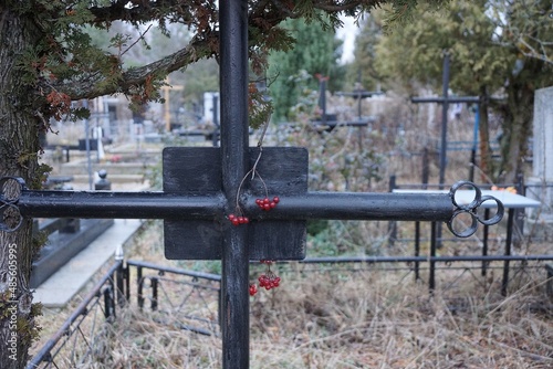 one black metal cross on a grave in dry gray grass in a cemetery