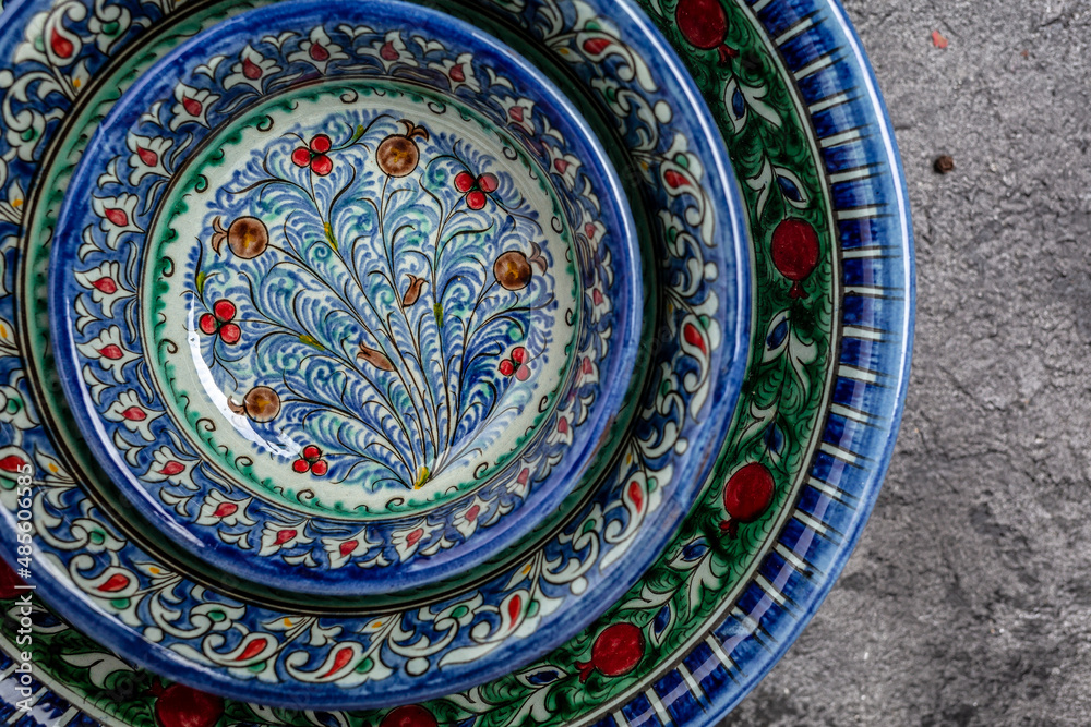 Naklejka premium Three hand painted blue ceramic dishes, traditional Uzbek utensils dishes, bowl, plates with national floral ornament on dark background, Long banner format. top view