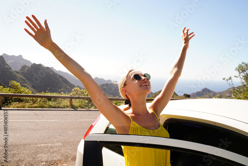 Happy smiling woman enjoying a car road trip along the mountainous landscape during sunrise, off-road trip.