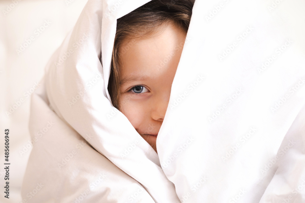 A little blue-eyed girl hides in a white blanket and peeks out. Close-up. Morning. Bedroom. A new day. Lifestyle. A little blue-eyed girl hides in a white blanket and peeks out. Close-up. Morning. Bedroom. A new day. Lifestyle.