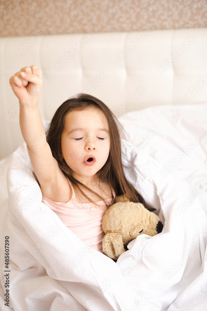 A pretty little girl woke up in her bed and stretches and yawns in the bedroom in the morning. A new day. Lifestyle. A pretty little girl woke up in her bed and stretches and yawns in the bedroom in the morning. A new day. Lifestyle.