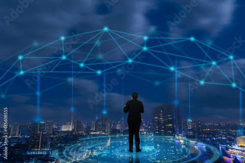 Professional businessman standing on smart city, wireless network and futuristic interface graphic at city night on background, Business technology concept.