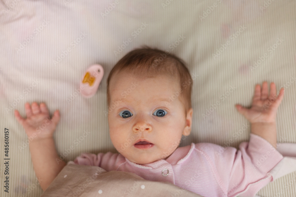 The baby looks in bed in surprise. Nipple nearby The baby looks in bed in surprise. Nipple nearby