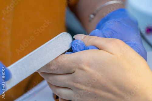 Close-up of a manicure master in blue gloves filing nails with a special nail file. Nail treatment process