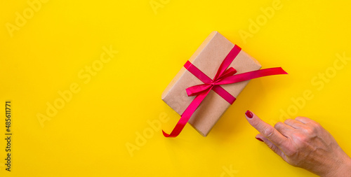 Woman hand, gift with red ribbon, yellow background.