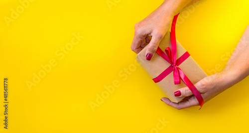 Woman hands holding gift, yellow background.