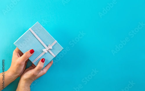 Woman hands holding gift, blue background.