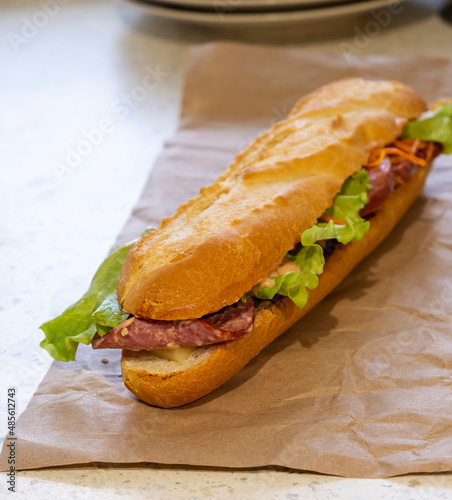 Large baguette sandwich with salami, lettuce, cheese and sauce. Selective focus.