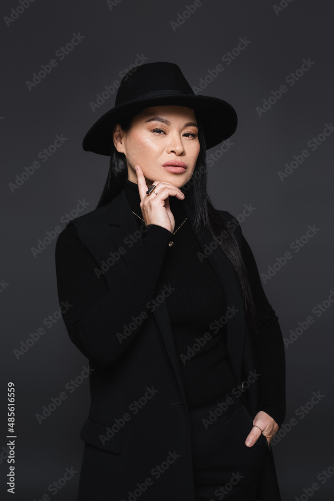 Stylish asian model in fedora hat posing isolated on dark grey Stylish asian model in fedora hat posing isolated on dark grey