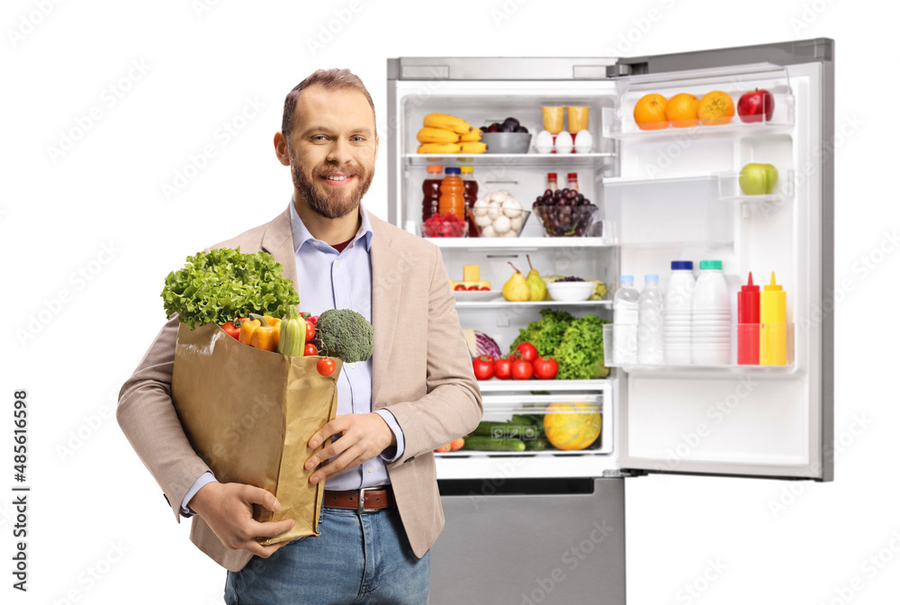 Young casual man holding a grocery bag in front of an open fridge Young casual man holding a grocery bag in front of an open fridge