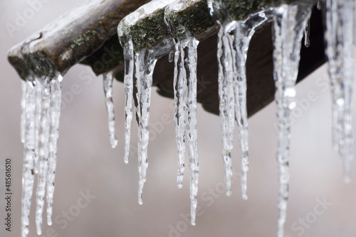 The icicles are melting from eave of roof. Thaw and end of winter. Drops of water slowly fall of a roof. Blurred background and bokeh. © imartsenyuk