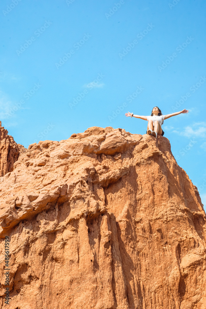 Low level shot of caucasian woman sitting in a rock and open arms with clear sky. wilderness