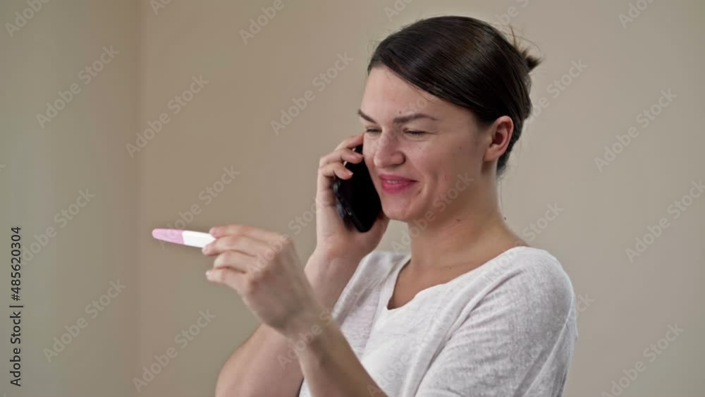Happy woman holding her positive result on pregnancy test and talking by a smartphone with the family. Happy woman holding her positive result on pregnancy test and talking by a smartphone with the family.