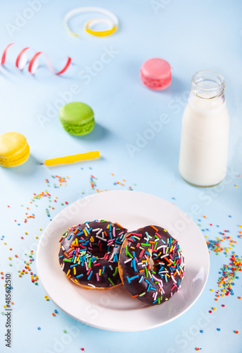 Delicious donuts with chocolate icing and birthday candle with bottle of milk and macaroons on the background.