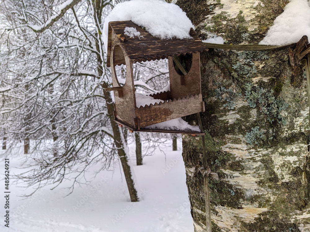 Naklejka premium old and broken wooden birdhouse hanging on a tree in the park in the winter season covered with snow.