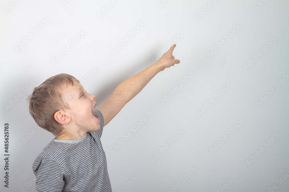 A Caucasian boy in a gray T-shirt shows his fingers to the side and looks at something with surprise and joy A Caucasian boy in a gray T-shirt shows his fingers to the side and looks at something with surprise and joy
