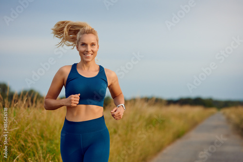 Fit healthy young woman enjoying a jog along a country road passing the camera with a happy smile full of vitality in an active lifestyle concept