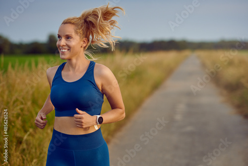 Fit healthy young woman enjoying a jog along a country road passing the camera with a happy smile full of vitality in an active lifestyle concept