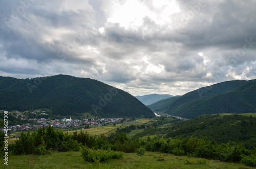 Beautiful summer view of rural landscape with typical mountain village on the valley and mountain range on background. Carpathians, Ukraine