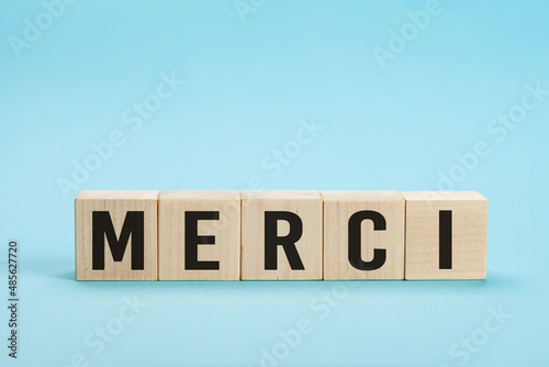 Merci - Thank you in French language. Merci Word on Letter Tiles on blue Background. Minimal aesthetics. Word merci thank you in french on wooden cubes