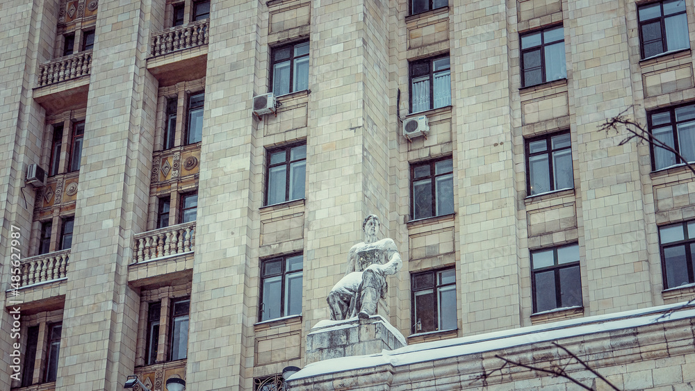 Statue of a man against the backdrop of a multi-storey building, photo during the day