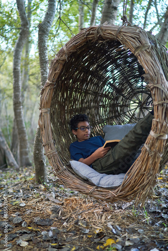 Boy reading book in nest swing in woods photo