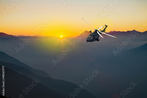 military helicopter flying over the alps at sunset