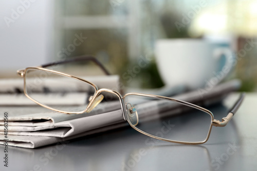 Stack of newspapers and glasses on grey table indoors, closeup