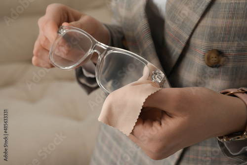 Woman cleaning glasses with microfiber cloth at home  closeup