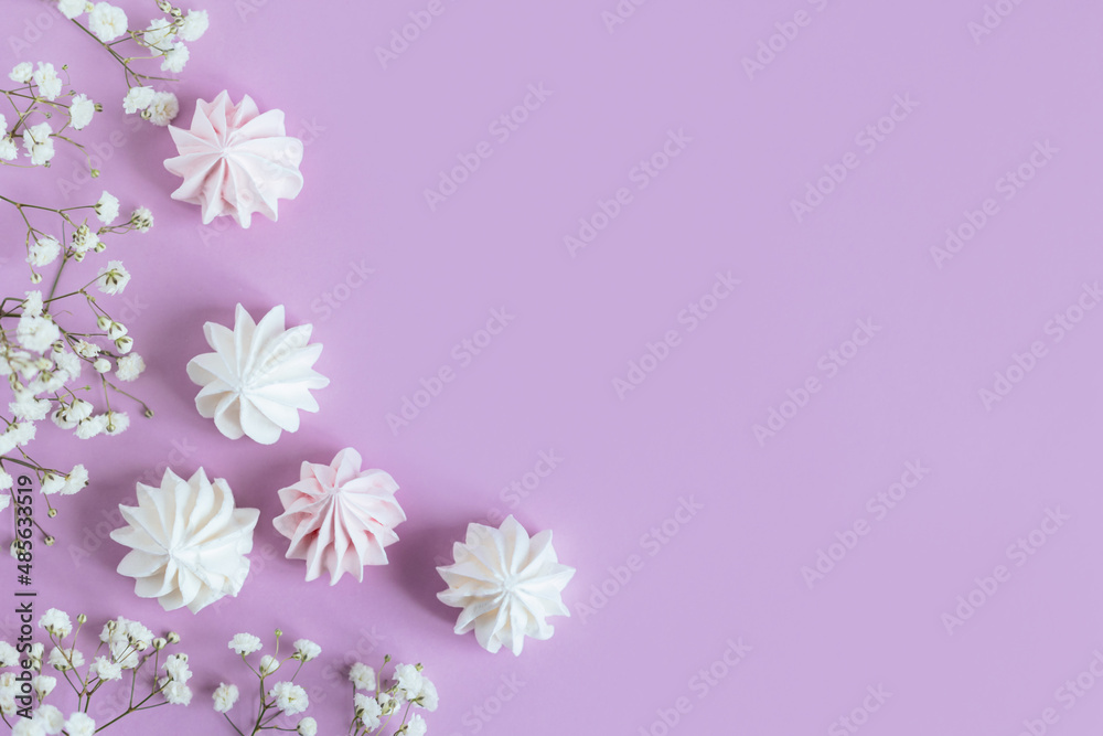 White marshmallows and flowers on a violet pastel background.