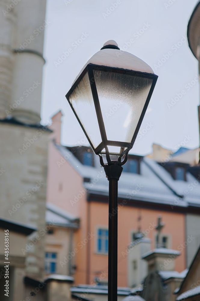 An old glass vintage lantern with snow in the historical center of Lviv on blue sky background. The concept of winter city.