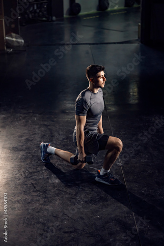 A sporty man doing lunges with dumbbells in a gym 
